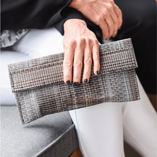 Woman sitting and holding a colorful, mesh clutch bag. 