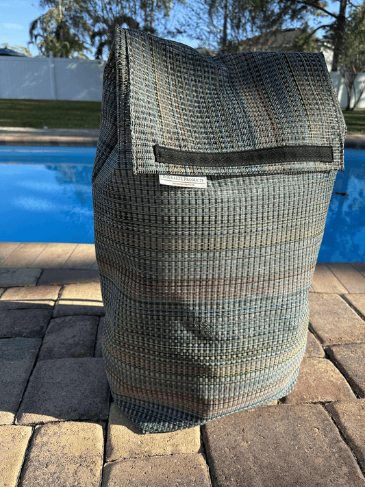 Rainbow mesh sports bag sitting on brick in front of a swimming pool.