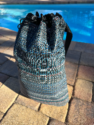 Colorful sports bag sitting outside on brick in front of a swimming pool.