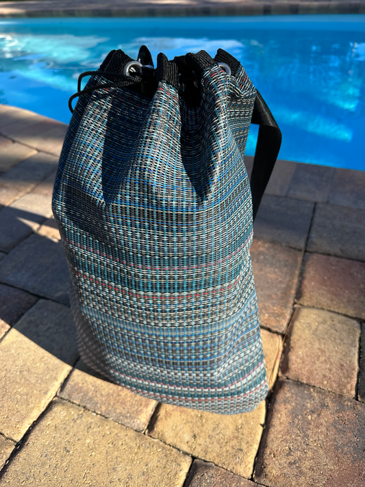 Colorful sports bag sitting outside on brick in front of a swimming pool.