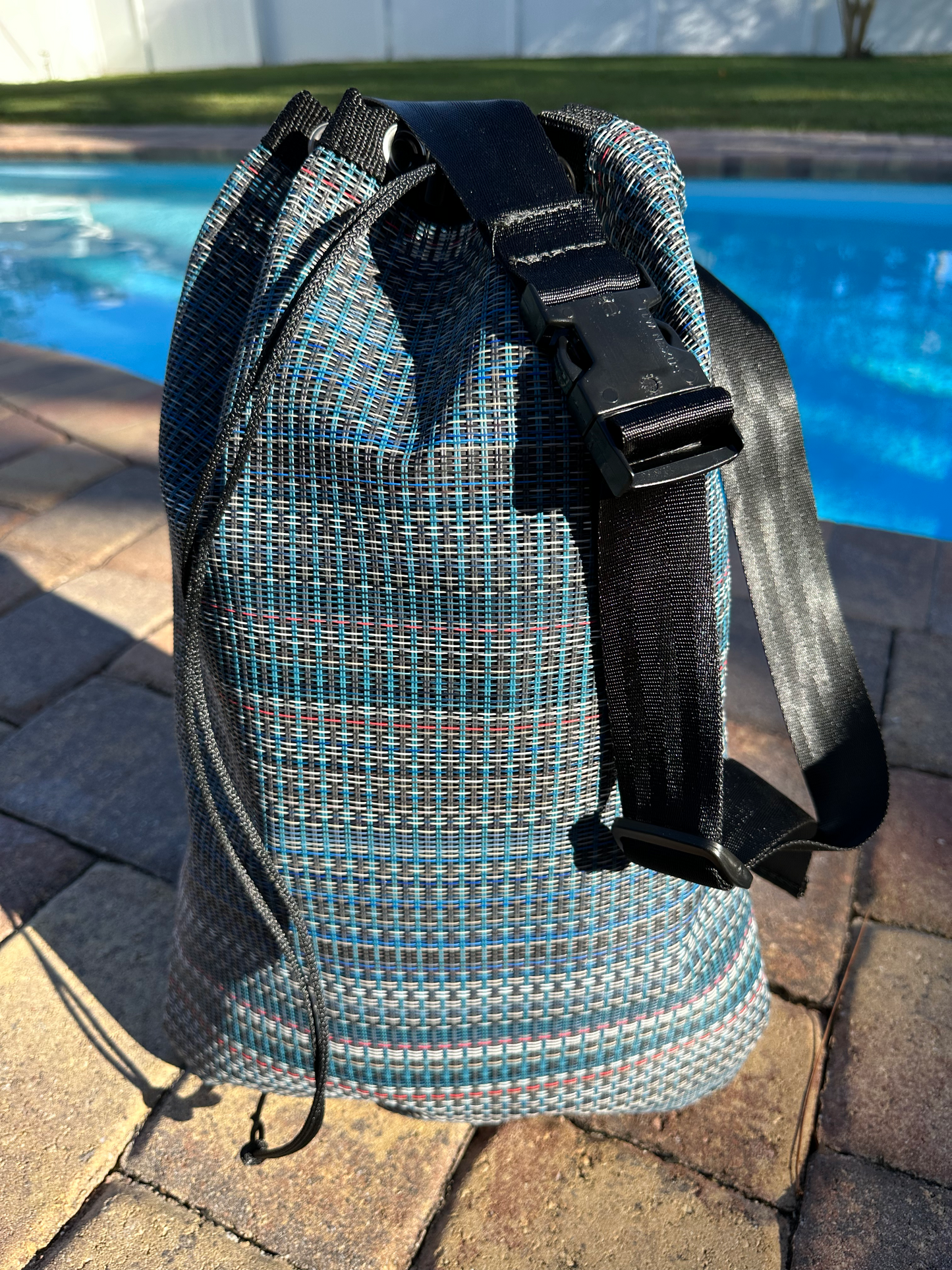 Colorful tote bag sitting outside on brick in front of a swimming pool.